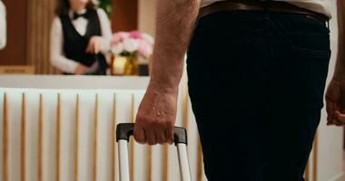 Retired person approaching front desk at hotel, carrying luggage before check in formalities. Tourist talking to employees about all inclusive services, retirement vacation. Close up. Handheld shot. photo