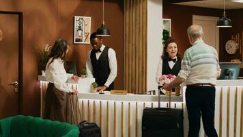 Retired couple arrive at hotel reception, talking to front desk staff before working on check in process. Tourists with luggage travelling on holiday to have fun, hotel concierge luxury services. photo