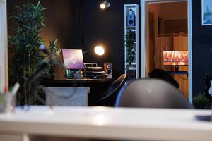 Work desk with computer and house plants in dimly lit empty home studio interior. Apartment illuminated by RGB lights with 3D rendered animations running on powerful PC monitors photo