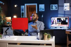 Man filming sponsored content, holding empty copy space sign in hand, following given script while talking to audience. Media star using cardboard bubble speech cutout to do promotion to viewers photo