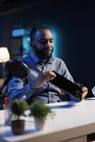 Tech engineer presenting tablet in entry level low budget price range, filming from dimly lit home studio. Viral tech content creator reviewing digital device in front of online audience photo