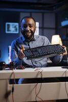 African american content creator analyzing mechanical keyboard received from sponsor, doing honest review for online streaming channel. Internet show host reviewing computer peripherals brand photo