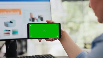 Analyst examines greenscreen software while she holds smartphone, isolated copyspace template shown on screen. Specialist checking blank mockup layout on mobile device. Handheld shot. Close up. photo