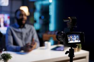 Focus on professional camera capturing footage of BIPOC man chatting with online audience. Viral content creator in blurry background talking with fans, filming with high quality recording tech photo