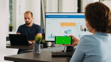 Office worker looks at greenscreen on smartphone display app, analyzing isolated chromakey layout on mobile device at work. Woman holding phone that shows blank mockup template. photo