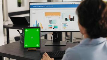 Manager watches tablet with greenscreen while she solves business operations in office, looking at device running blank mockup display. Specialist looks at chromakey software. Handheld shot. photo
