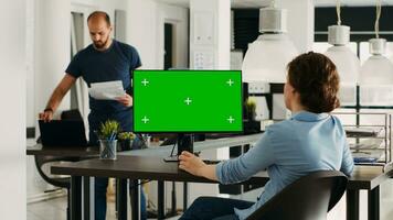 Specialist looking at greenscreen template on desktop monitor in small business agency workplace. Person checking isolated display showing blank chromakey mockup, problem solving. Tripod shot. photo