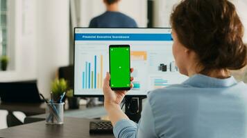 Worker holding device with greenscreen at agency office workstation, startup manager examining isolated mockup template on smartphone. Woman working with blank chromakey layout. photo