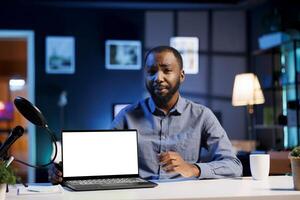 African american tech expert presenting mockup laptop in entry level low budget price range. Viral content creator reviewing isolated screen notebook in front of internet fanbase photo