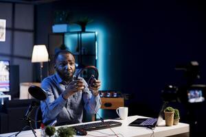 Internet show host holding pair of expensive headphones in hands, doing giveaway for loyal viewers from his home studio. Content creator hosting online contest for fans with audio tech as prize photo