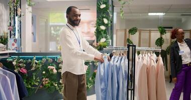 Smiling retail assistant arranging clothes in mall clothing store with fast fashion attire following the latest trends. Cheerful worker organizing assortment of elegant men blazers in fashion boutique photo