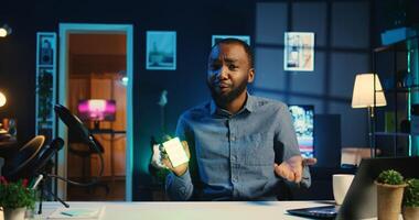 African american tech content creator filming technology review of mini RGB lights device illuminating in different colors. Viral internet star showing helpful broadcast production tool to subscribers photo