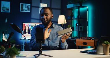 Content creator in studio films Bluetooth speaker video review for tech enthusiasts. African american viral online star hosts technology internet show, unboxing portable audio system photo