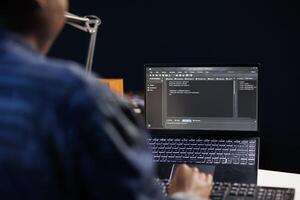 African American developer managing a system, typing on keyboard and laptop screen showing software programming. Professional freelancer working on data center and network security. photo