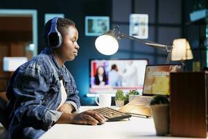 Black woman with headphones sits in front of wireless computer, which is showing game over. Female player is staring at her digital laptop screen while wearing a headset and losing a game. photo