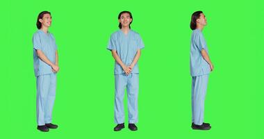 Young nurse specialist posing on camera with confidence, wearing hospital attire and standing with arms crossed against full body greenscreen. Medical assistant having healthcare expertise and skill. photo