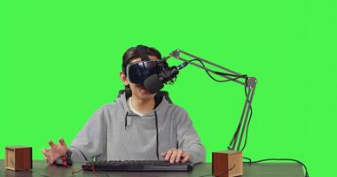 Video blogger streaming live gameplay at workstation, playing online competition with virtual reality headgear. Asian person broadcasting videogames stream, content creator on greenscreen. photo