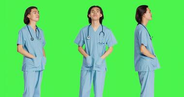 Nurse taking stethoscope and getting equipped with medical uniform, preparing for healthcare check up at clinic. Asian specialist using instrument against greenscreen backdrop. photo