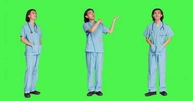 Working in medical industry, male specialist doing ad commercial against full body greenscreen backdrop. Medic in blue uniform points to left or right sides, presenting marketing advertisement. photo