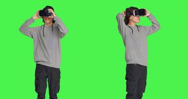 joven adulto disfruta virtual realidad tecnología en estudio con pantalla verde fondo, utilizando interactivo 3d visión en auriculares. moderno chico teniendo divertido con artificial inteligencia vr lentes. foto