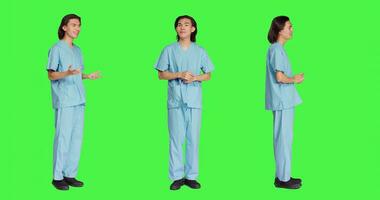 Cheerful nurse waving in studio and greeting sick people, standing over full body greenscreen backdrop. Medical specialist assistant being respectful and friendly with patients, healthcare uniform. photo