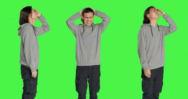 Unwell person dealing with migraine, rubbing temples and feeling worried about painful headache. Young man being in pain, sick adult with the flu over isolated greenscreen in studio. photo