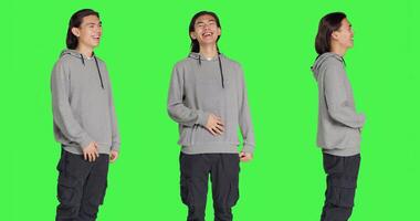 Positive man laughing on camera, posing feeling cheerful against greenscreen backdrop. Asian person smiling in studio, expressing amusing funny gestures, relaxed optimistic guy. photo
