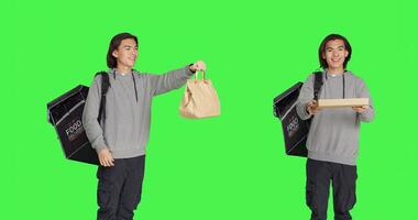 posicionado terminado pantalla verde estudio fondo, asiático hombre trabajando en entregando comida con mochila. joven persona que lleva envase para entrega servicio, ansioso a proporcionar pedidos de alimento. foto