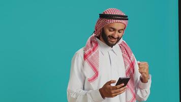 Arabic person in traditional outfit holding smartphone in hands and typing in online social media chat. Muslim adult standing with mobile phone and texting on webpage, internet site. photo