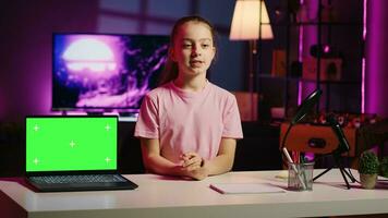 Cute kid in home studio presenting advertisement from sponsoring brand on green screen laptop. Young girl using chroma key device to present promotion from media partner to audience photo