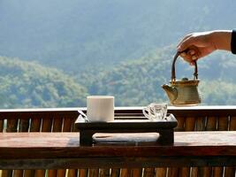 A hand pouring tea from glass teapot on wooden serving tray, hands pouring tea from teapot, Cropped shot of pouring tea in traditional chinese tea ware photo