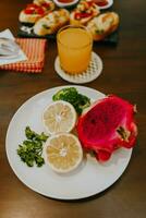 Appetizer table with Italian antipasti snacks and orange juice in glasses. Fresh lemon and dragon fruit on white plate. Brushetta or authentic traditional Spanish tapas set over wooden table. photo