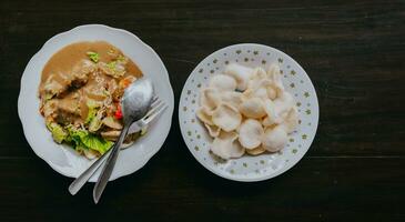 Top view of Javanese vegetable salad with peanut sauce gado-gado served with egg and shrimp cracker. Black wooden background. photo