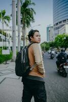 Asian male tourist traveling alone taking backpack in urban area. Palm trees and urban. Travel and vacation concept background. photo