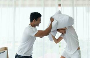 Beautiful couple having fun by fighting with a pillow on bed after waking up in bright bedroom. photo