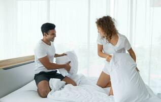 Beautiful couple having fun by fighting with a pillow on bed after waking up in bright bedroom. photo