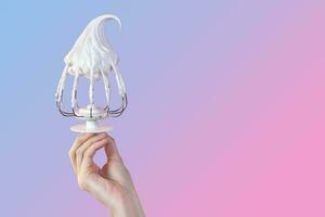 Woman's hand hold Whisk with cream, whisk with meringue cream isolated on gradient pink and blue photo copy space for text