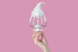 Woman's hand hold Whisk with cream, whisk with meringue cream isolated on pink photo