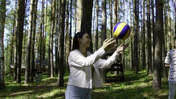 Group of friends is having fun playing volleyball. Stock footage. Friends are playing volleyball in forest clearing. Friends in circle play volleyball in forest on sunny summer day photo