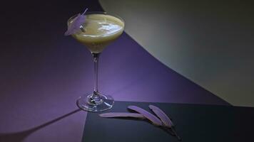 Refreshing alcoholic drink in martini glass. Stock footage. Close up of beverage served on lilac and white surface and decorated with small purle feathers. photo