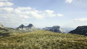 Top view of mountain panorama against blue sky. Stock. Rocky peaks of mountains with cover of grass at foothills create beautiful landscape photo