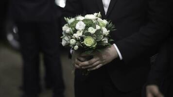 Handsome businessman holding flowers. Groom in a suit holding a bouquet of flowers. Wedding boutonniere. Elegant man dressed in a modern black suit and white shirt holding in hand a wedding flowers photo