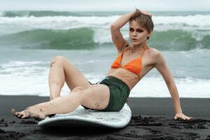 Female surfer sitting on surfboard, she looks so authentic and genuine, and even gazing at camera photo