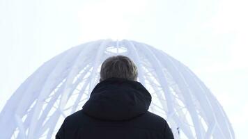 Back view of man looking at dome building. Media. View from back of man considering architectural structure of open dome against sky photo