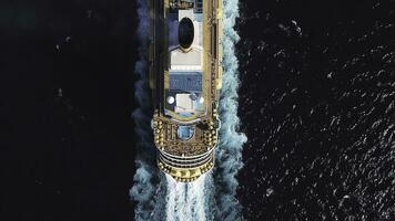 Bird eye top view of large cruiser ship in deep blue water in a sunny day, luxury concept. Stock. Aerial view of luxury cruise liner with swimming pools and basketball field on board at blue ocean. photo