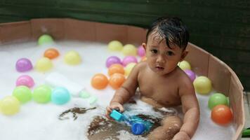 carino bambino avendo divertimento assunzione bagno giocando nel acqua con schiuma con colorato giocattoli. video