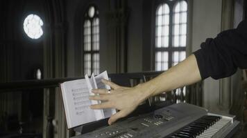 hombre con sábana música y piano. acción. hombre voltea mediante música libro en sintetizador. de cerca de músico en sintetizador en Iglesia foto