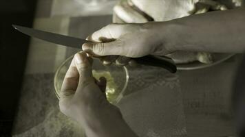 cerca arriba de hembra corte ajo con un cocina cuchillo. acción. parte superior ver de mujer manos corte ajo y lanzamiento eso dentro el vaso profundo plato en pie en el mesa, Cocinando concepto. foto