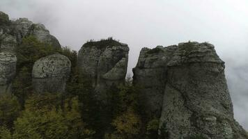 View near stone pillar of cliff. Shot. Top view of stone pillar of rock with approaching thick fog. Autumn landscape with colorful shrubs and dense gray fog on mountain photo