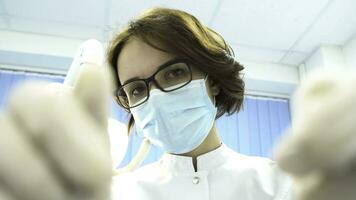 First person view of a young female dentist in mask approaches with Tools. Media. Young doctor standing over the patient, looking at camera. photo